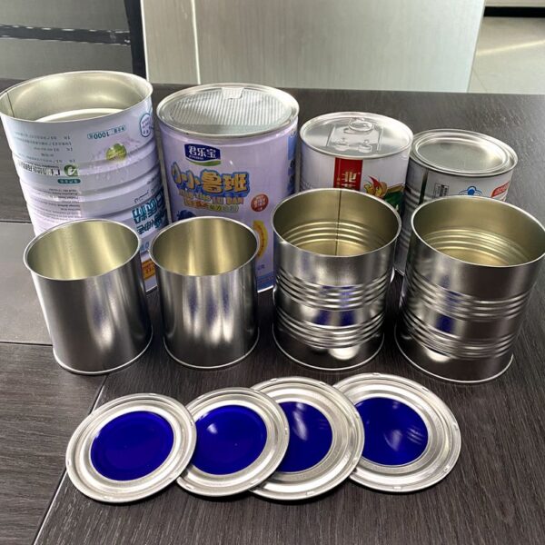 Assorted empty metal cans of varying sizes on a dark surface, with round blue-lidded lids in front.